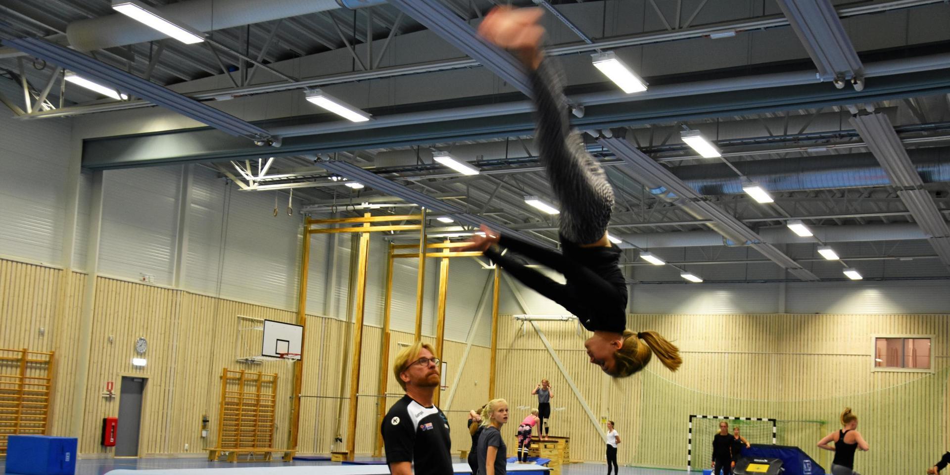 En gymnast är raklång, upp-och-ner i luften medan en tränare ser på